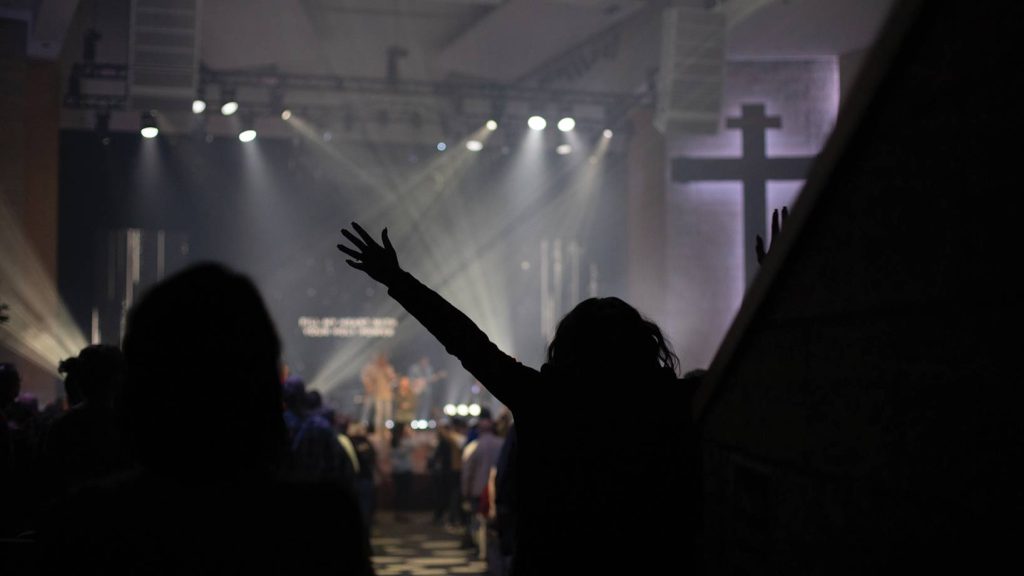 Lights dim during Worship Night with the silhouette of a woman raising her arms in worship
