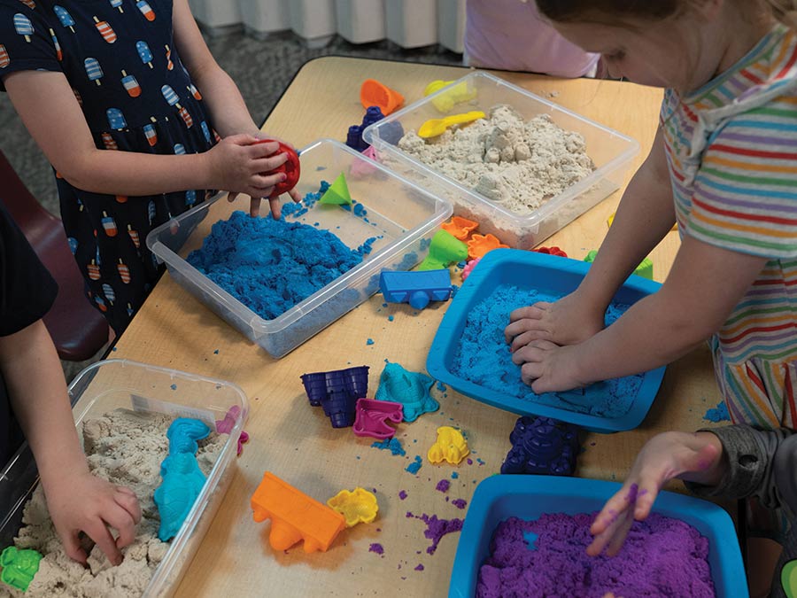 A table full of kinetic sand bins and little hands playing