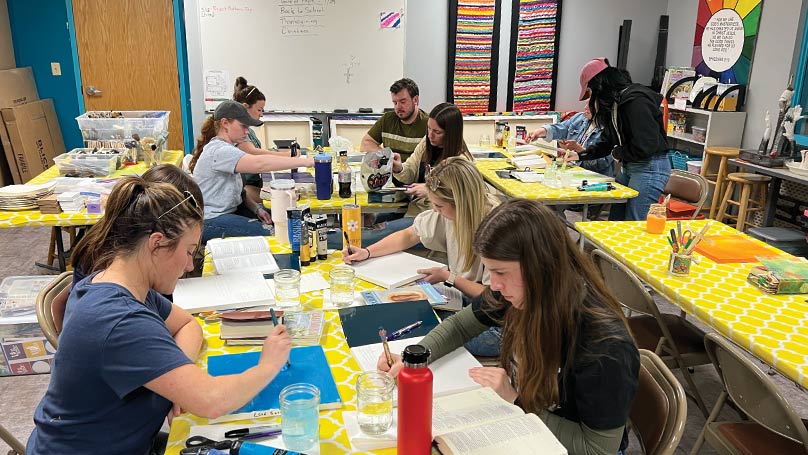 People painting canvases at tables in a room with colorfully decorated walls