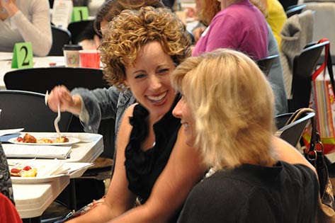 Two women chatting among a larger group at a women's event