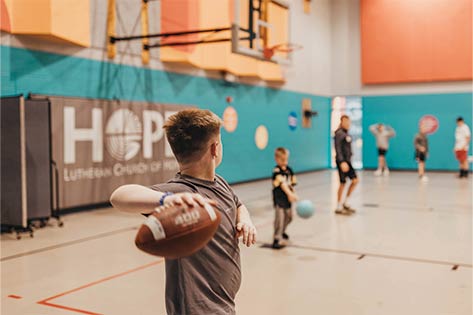 Kids playing various in the gym; boy throwing football in the foreground