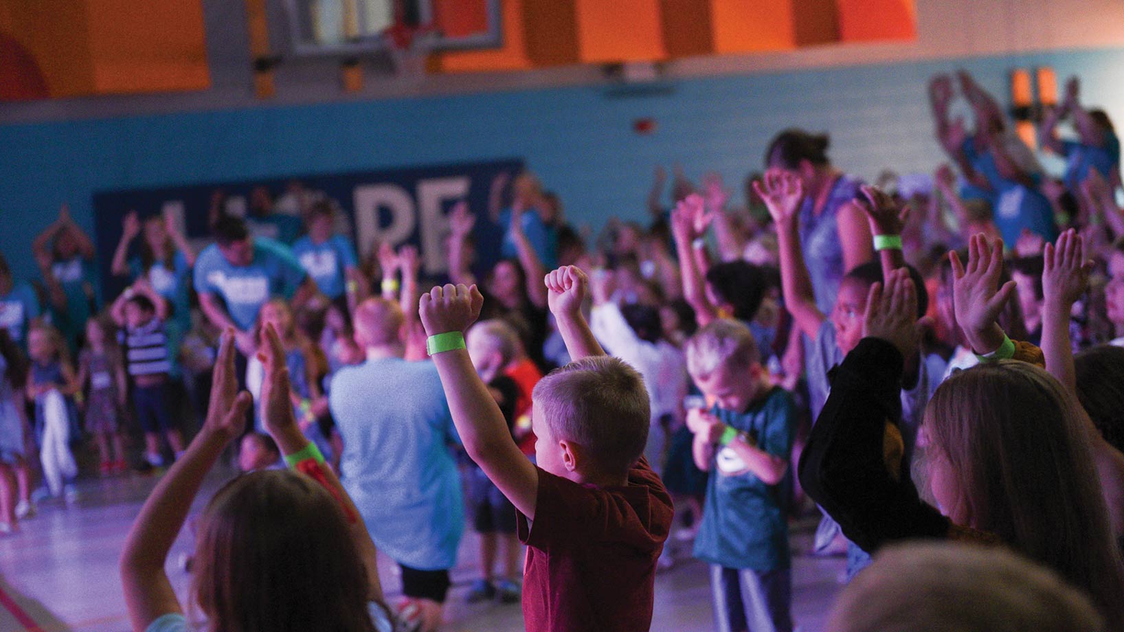 Kids with arms raised dancing in the gym with lights glowing