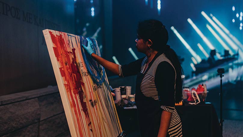 Woman painting a colorful canvas on stage with blue stage lights and the worship team in the background
