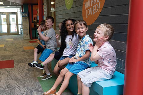 Preschool kids sitting and smiling on bench in a hallway