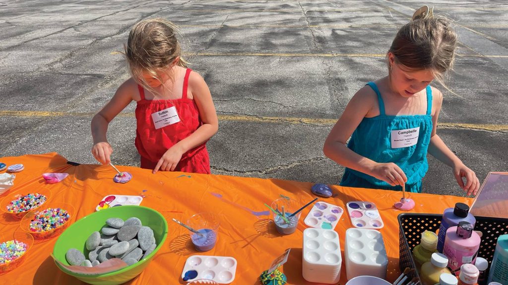 Two girls playing at a colorful craft table outside