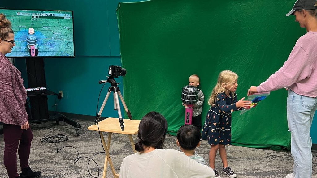 Kids playing in front of a green screen, pretending to be meteorologists.