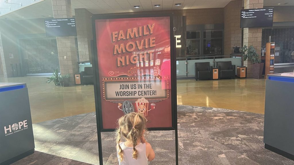 Little girl excitedly looks at Family Movie Night sign in New to Hope area.