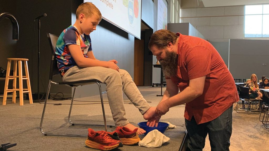 Pastor Ben washing young boy's feet on stage.
