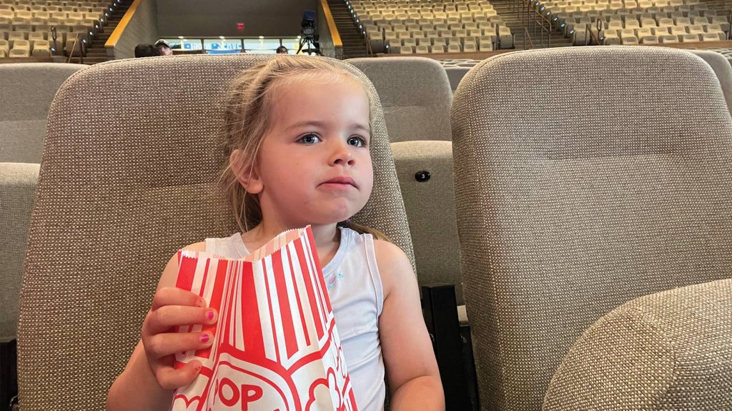 Little girl holding bag of popcorn watching movie in Worship Center.