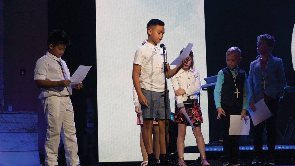 Young boy reading off of paper on stage.