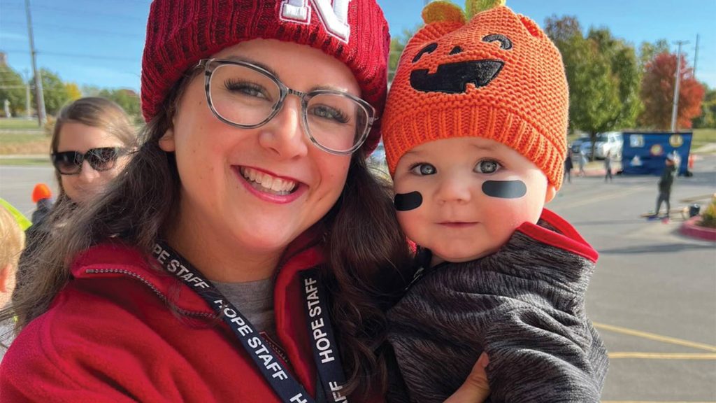 Mom and toddler son pose for a photo. Little boy has on a pumpkin hat and eye black.