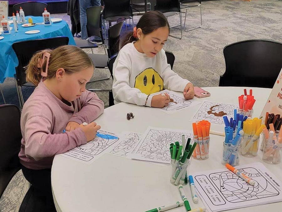 Two girls coloring at a table with coloring sheets and markers