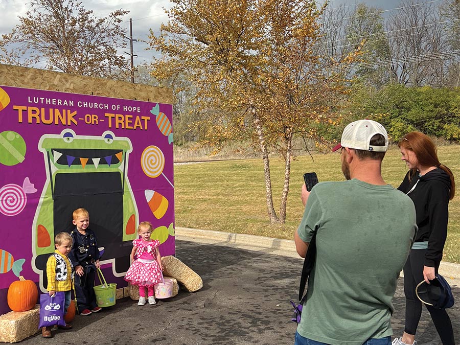 Kids dressed in costumes posing in front of Trunk or Treat photo backdrop while parents take photos.