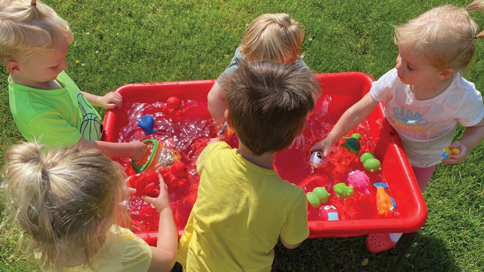 Group of kids playing in water sensory tub on grass