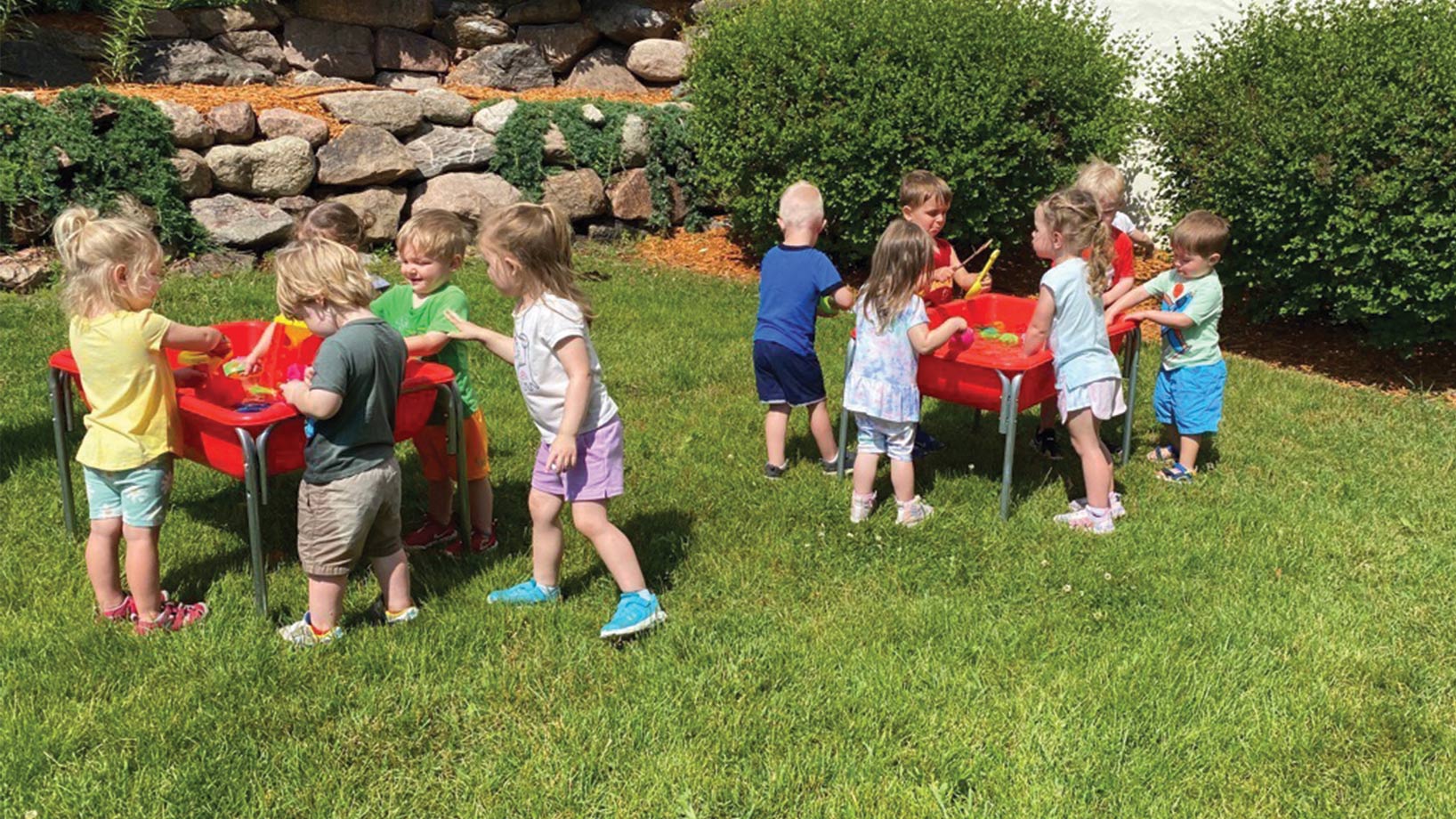 Class of kids playing outside in water sensory bins on grass