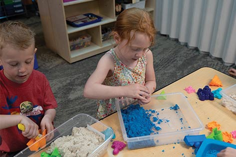 Two kids play with sensory sand in preschool classroom