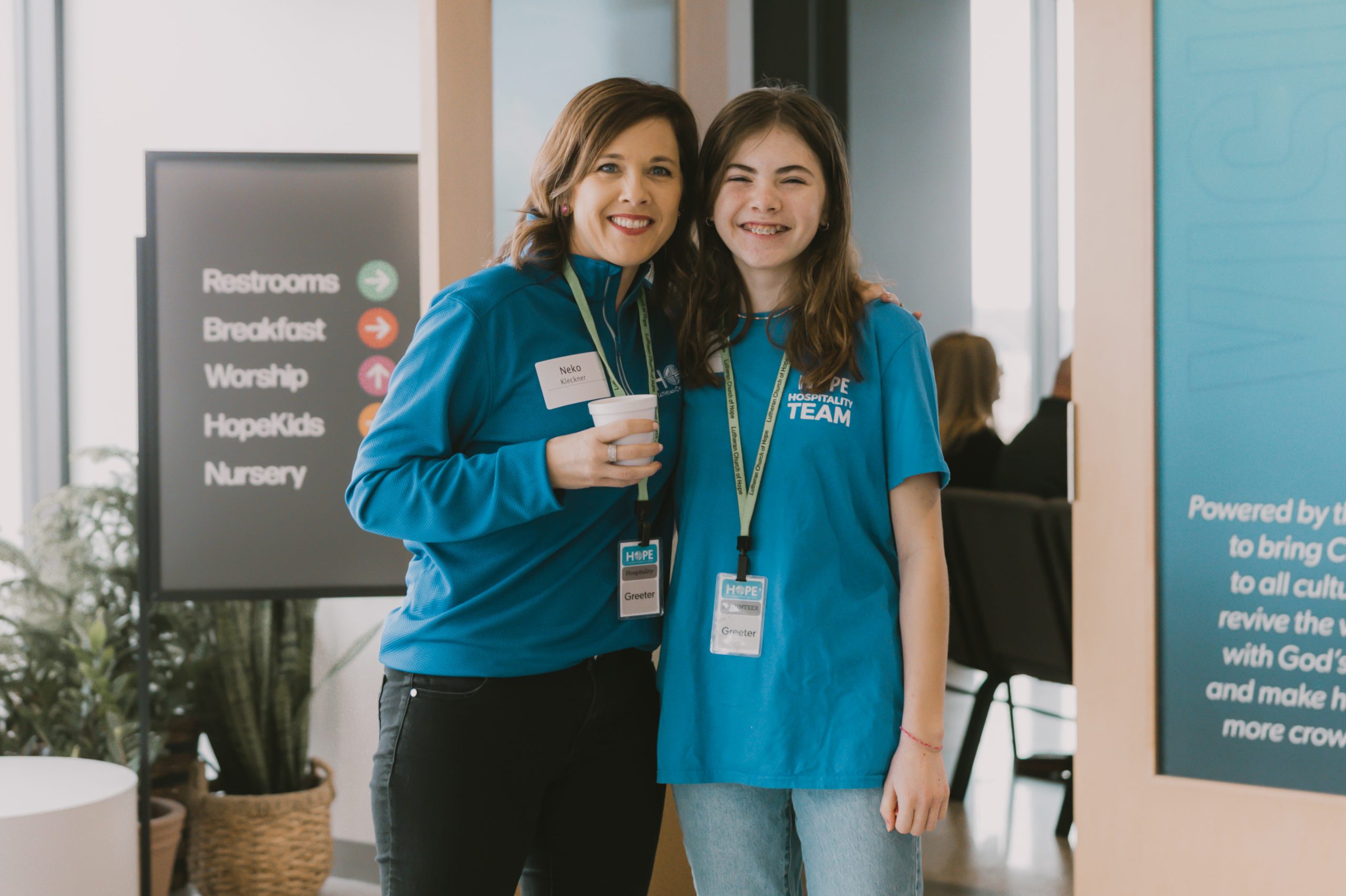 Mother and daughter wearing blue Hospitality Team shirts during volunteer shift during church service